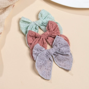 Détail de nœuds en coton brodés ajourés en vert menthe, rose poudré et lavande pâle