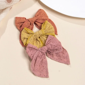 Détail de trois barrettes à nœuds en coton brodé avec motifs floraux ajourés et longs rubans