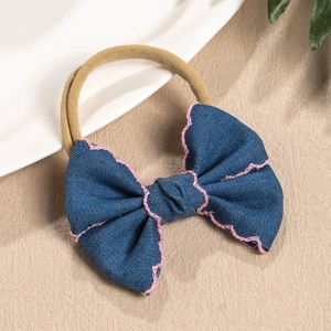 Detail of baby headband with denim blue bow and pink wavy stitched edges on nylon band