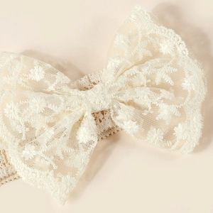 Détail d'un bandeau bébé en dentelle avec nœud brodé ivoire et bande tricotée souple