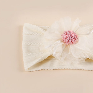 Soft white knit baby headband with large pink jacquard mesh flower on beige background
