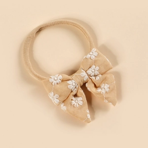 Détail du bandeau bébé avec broderie florale blanche sur un nœud en coton beige