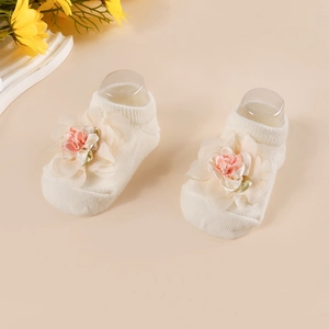 Detail of infant socks with 3D fabric flowers in cream and pink on a beige background