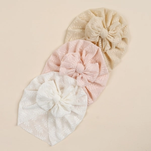 Detailed macro view of three lace baby turbans with elegant floral embroidery and bows
