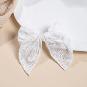 Détail d'un nœud à cheveux en dentelle blanche avec broderie florale sur tissu beige doux