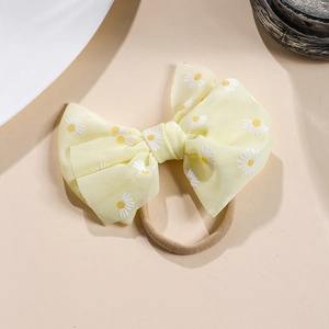 Detailansicht eines gelben Haarbands mit Netzschleife und zartem Gänseblümchen-Druck