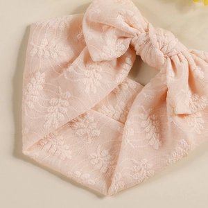 Détail d'un bandeau en dentelle pour bébé avec texture florale et gros nœud rose