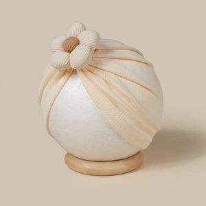 Gros plan d'un turban bébé beige en maille côtelée orné d'une grande fleur en 3D doux