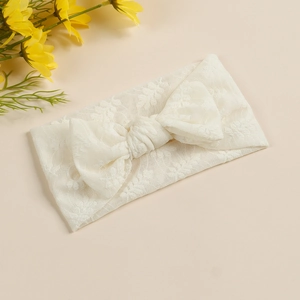 Vue détaillée de la broderie en dentelle blanche et du grand nœud sur le bandeau bébé