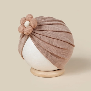Détail d'un bonnet turban en tricot rose poudré pour bébé avec une grande fleur en 3D