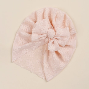 Close-up of baby lace turban in soft pink with intricate floral texture and large bow