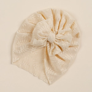 Detail of baby lace turban hat with large bow and intricate leaf mesh texture