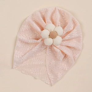Detail of baby pink lace turban hat with a 3D fabric flower on a beige background