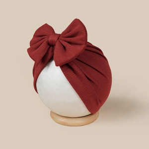 Detail of burgundy ribbed knit baby turban hat featuring a large bow on display stand