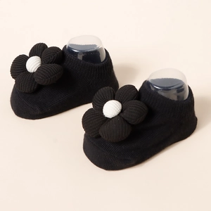 Close-up of black knit baby socks with 3D floral accents and white center detail