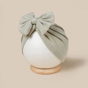 Detail of sage green knitted baby hat with a large bow on a soft beige background