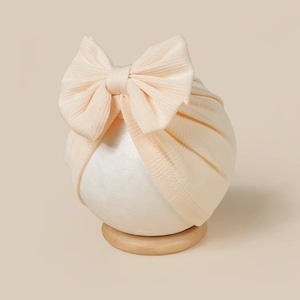 Close-up of baby turban hat with bow, featuring ribbed knit texture and soft beige color