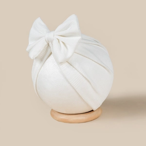 Detail showing white knit baby turban hat with a large decorative bow and soft texture