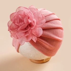 Détail du bonnet turban rose pour bébé avec une grande fleur décorative sur un modèle en mousse