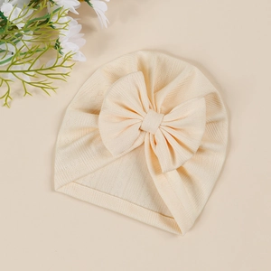 Detail of baby turban hat in cream knit fabric with a large decorative bow