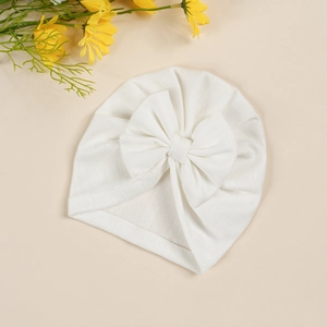 Detail of white knitted baby turban hat with a large bow showing soft rib texture