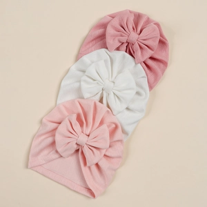 Detailed view of elastic ribbed knit baby hats with large bow accents in pink and white