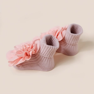 Détail de chaussettes en maille pour bébé ornées de grandes fleurs décoratives en tissu rose