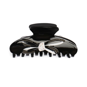 Détail d'une pince à cheveux noire en acrylique avec nœud en strass et bords dorés
