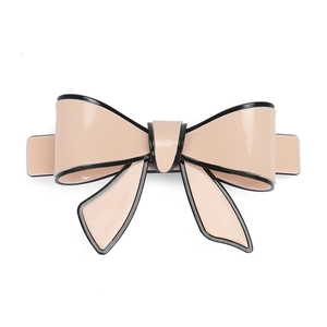 Detail of a glossy beige acrylic bow hair clip with black edges and spring fastener
