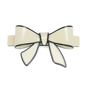 Detail of a beige bow hair clip with black edges and metallic spring fastening mechanism