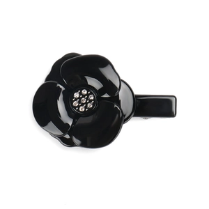 Detail of elegant black camellia hair clip with sparkling crystal center on white background