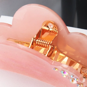 Detailed close-up of pink cloud hair claw clip with golden spring and rhinestones
