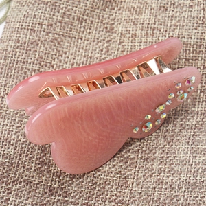 Detail of pink pearlescent acrylic hair claw with colorful rhinestones and gold teeth