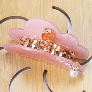 Macro detail of a pink cloud hair claw with gold spring and hanging pearl pendant