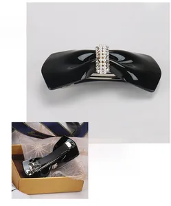 Detail of black bow hair clip with faux pearls and rhinestones on a metal spring clasp