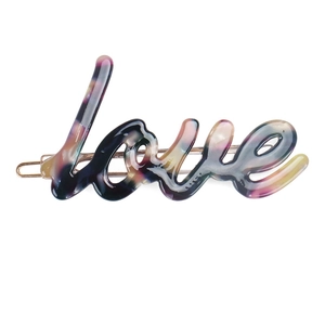 Detail showing 'Love' acetate hair clip with tortoiseshell texture and gold metal base