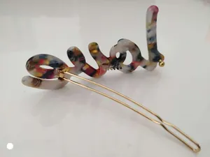 Close-up of golden hair clip featuring colorful marble textured 'LOVE' lettering design
