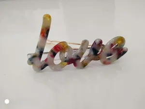 Close-up of a colorful acetate hair clip featuring a handwritten LOVE design and gold metal clip