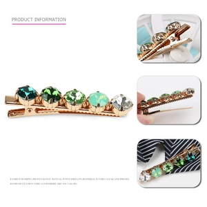Detailed macro view of the gold-tone metal duckbill hair clip with green crystal rhinestones
