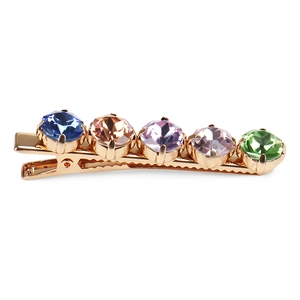 Close-up of golden alloy hair clip with five colorful crystals in blue, pink and green