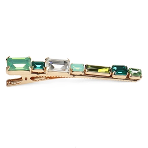 Close-up of golden hair clip with geometric green crystals and sparkling rhinestones