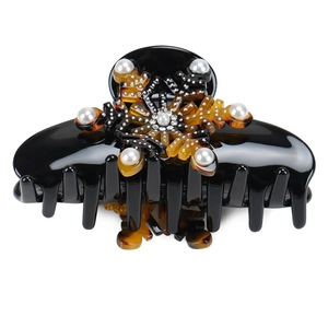 Detail of black acetate hair claw clip with amber snowflake motif and pearl accents