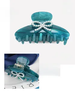 Detail of peacock blue acetate hair claw clip with pearl bow design and inner spring view