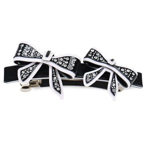 Detailed view of a black bow hair clip featuring white edges and sparkling crystals