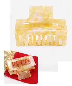 Detail of a square acetate hair claw clip with cream marble texture and metal spring mechanism
