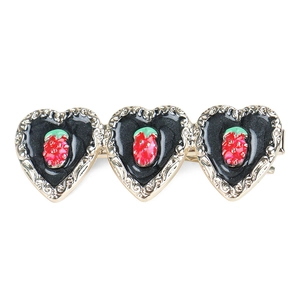 Detail of gold heart hair clip with black enamel finish and red strawberry charms