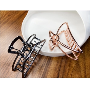 Close-up of geometric alloy hair claws in black and rose gold on wooden desk