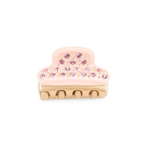 Mini hair claw clip with pink crystals and gold-tone metal base on light pink acetate