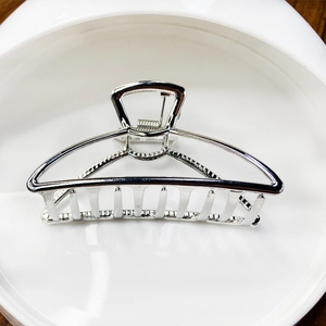 Polished silver alloy hair claw clip with hollow trapezoidal design on white tray