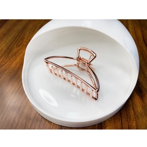 Polished rose gold alloy claw clip with hollow geometric design on a white ceramic tray